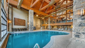 An indoor swimming pool with stone walls and wooden beams, surrounded by lounge chairs and a stone wall with a light fixture.