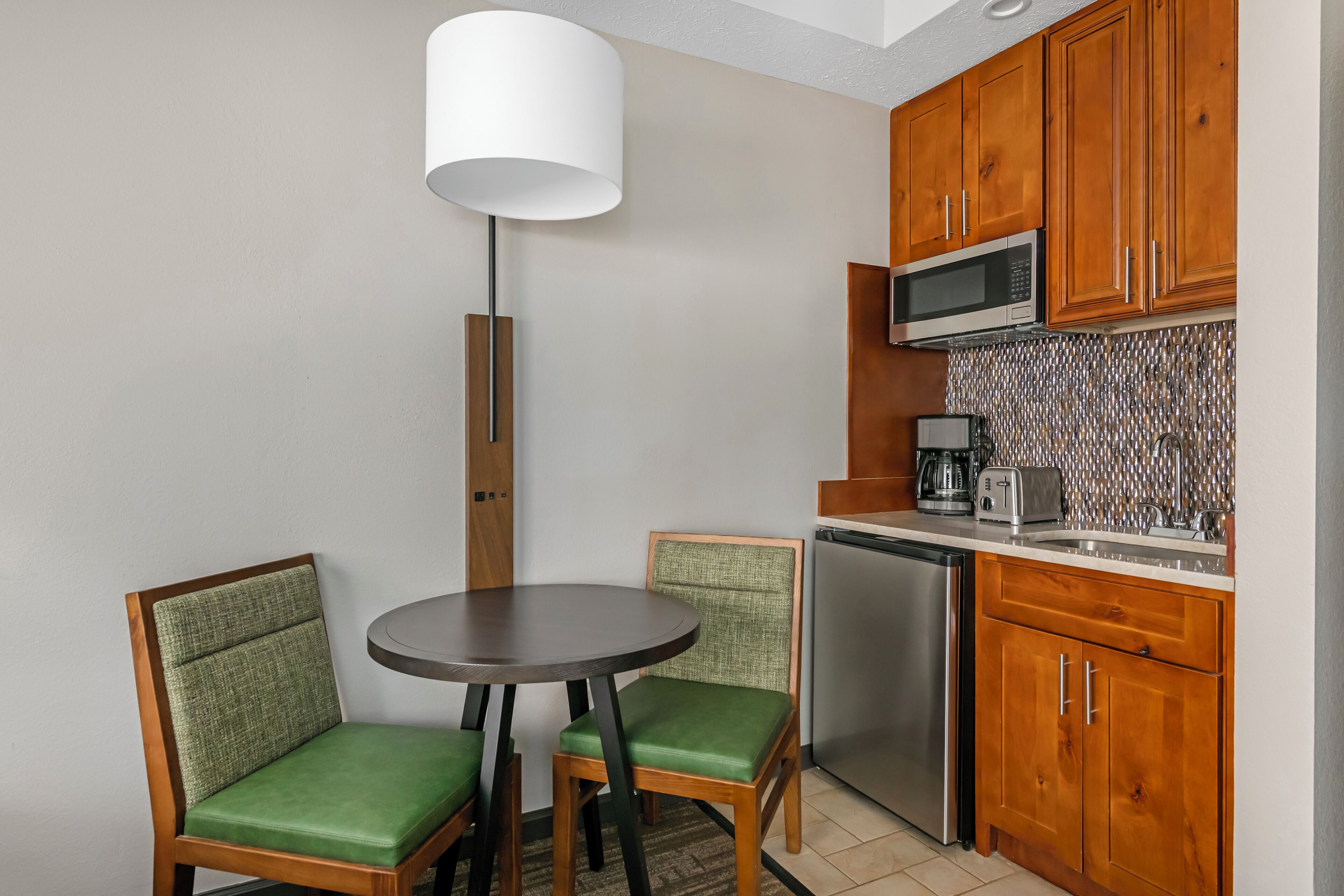 A compact kitchen with a microwave, toaster, and coffee maker. There is a dining table with two chairs.