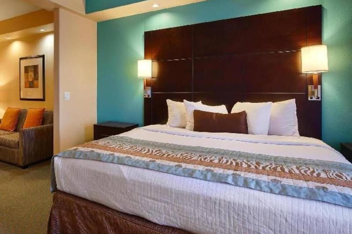Una habitación de hotel con una cama grande, cabecera, dos lámparas de noche, mesitas de noche y un sofá.