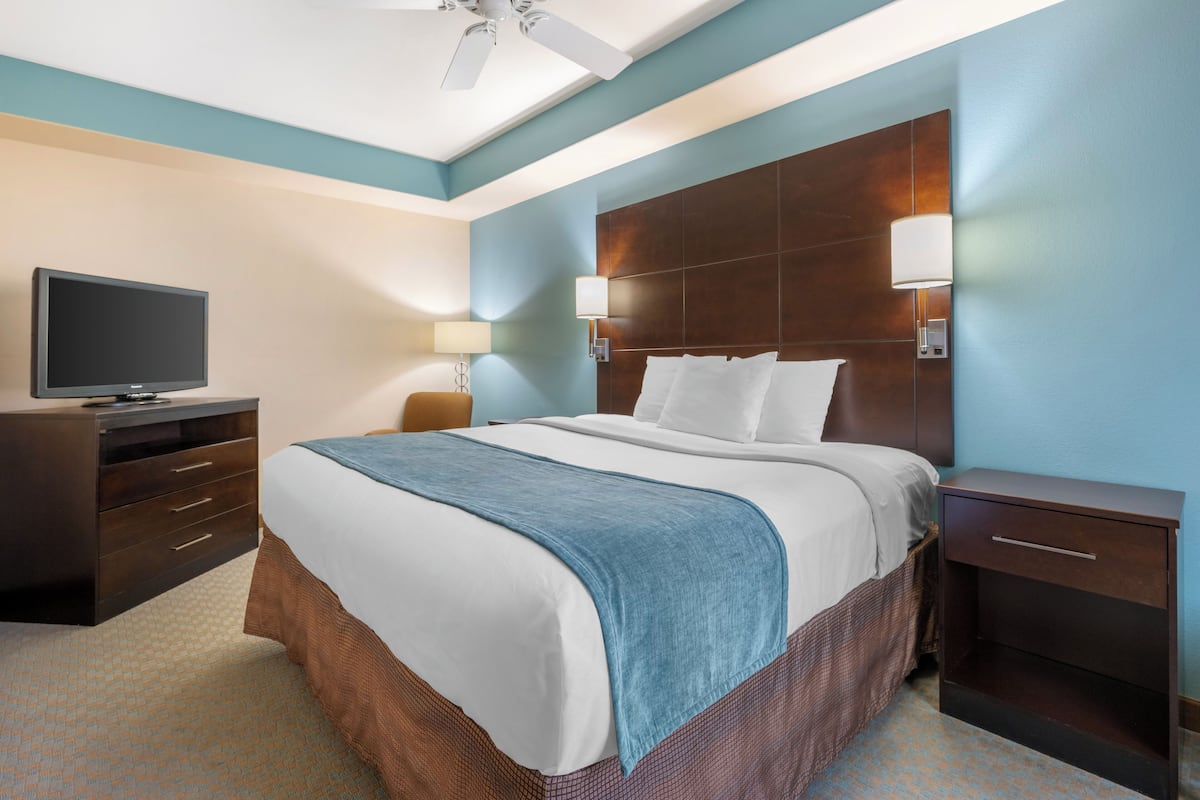 Una habitación de hotel con cama, televisor, mesita de noche y ventilador de techo.