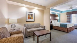 Una camera d'hotel con un divano, un tavolino, un letto con testiera, una ventola a soffitto e un quadro appeso al muro.