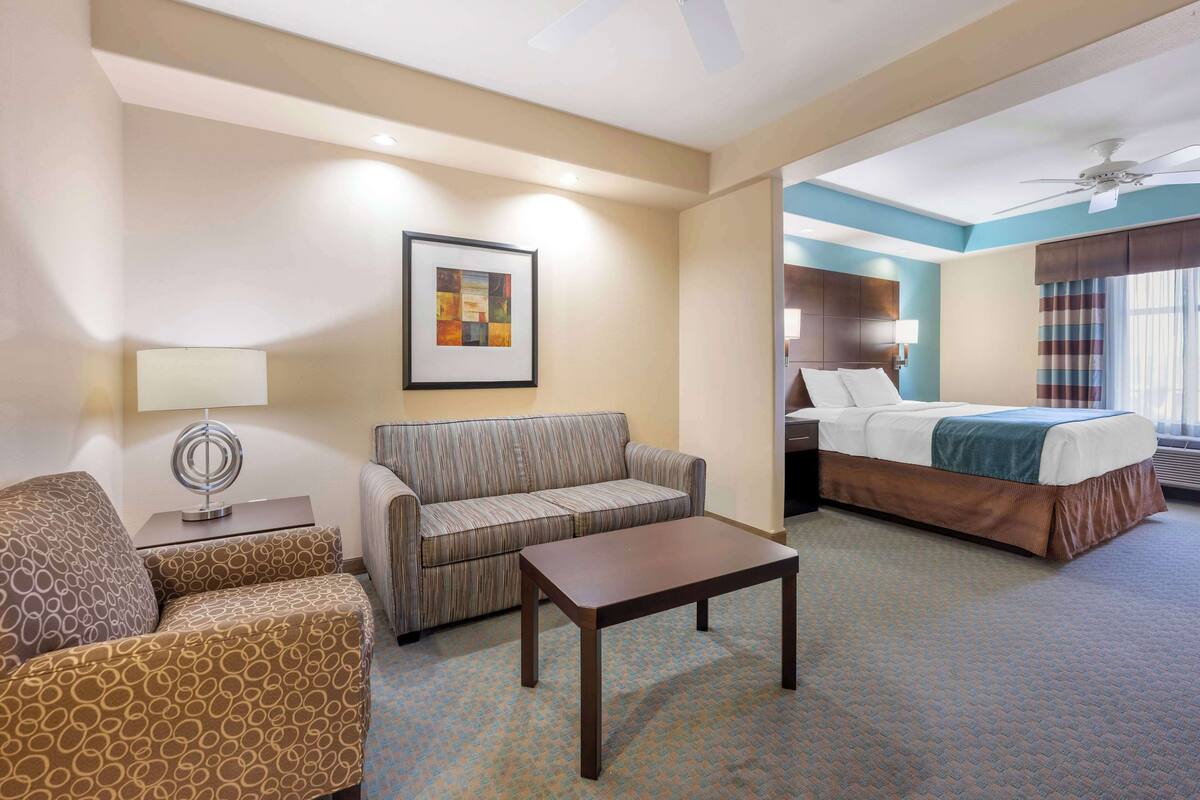 Habitación de hotel con sofá, una mesita, cama con cabecera, ventilador de techo y un cuadro en la pared.