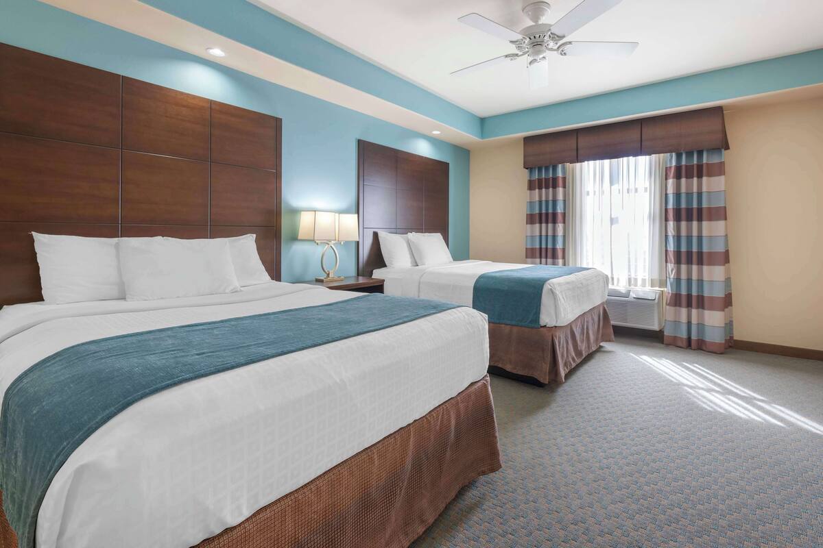Habitación de hotel con dos camas, un ventilador de techo y un ventanal con cortinas a rayas.