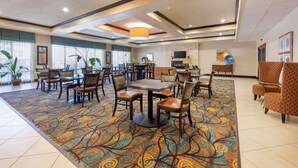 Un'ampia hall dell'hotel con una moquette fantasia, diverse zone relax e un televisore a parete.