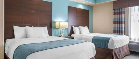 A hotel room with two beds, a large window with curtains, a ceiling fan, and a wall-mounted lamp.