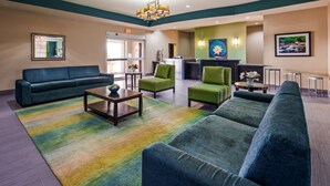 Un hall d’hôtel avec un canapé vert, un fauteuil vert, une table basse et un comptoir de réception.
