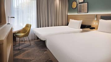 A hotel room with two beds, a desk, a chair, and a large window with curtains.