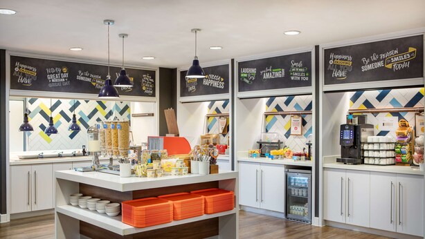 Un área de cocina moderna con una isla central, lámparas colgantes y decoración mural inspiradora.