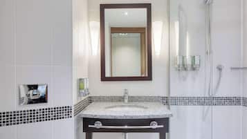 Un baño moderno con lavamanos de granito, un espejo grande y una ducha con mampara de vidrio.