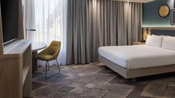 A hotel room with a bed, a desk, a chair, and a large window with curtains.