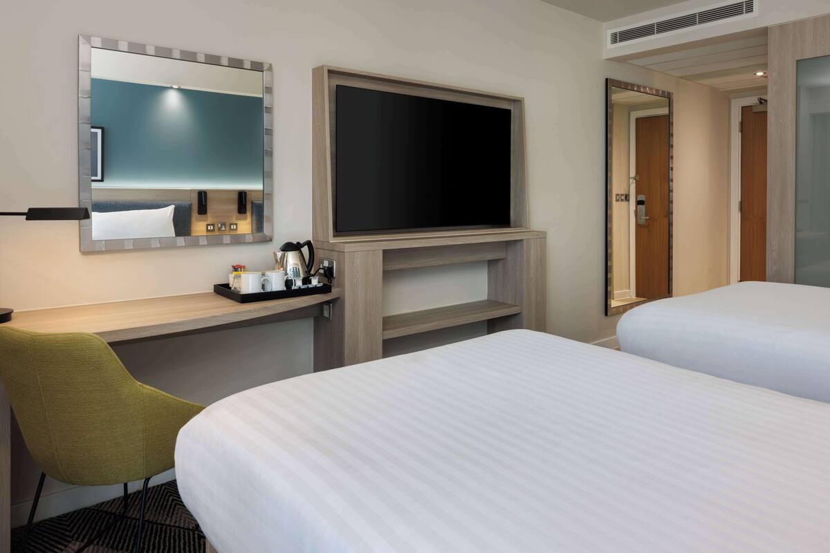 A hotel room with a bed, a desk with a chair, a flat-screen TV, and a mirror.