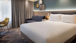 Habitación de hotel con una cama grande, un sofá, una silla y una mesita de noche con lámpara.