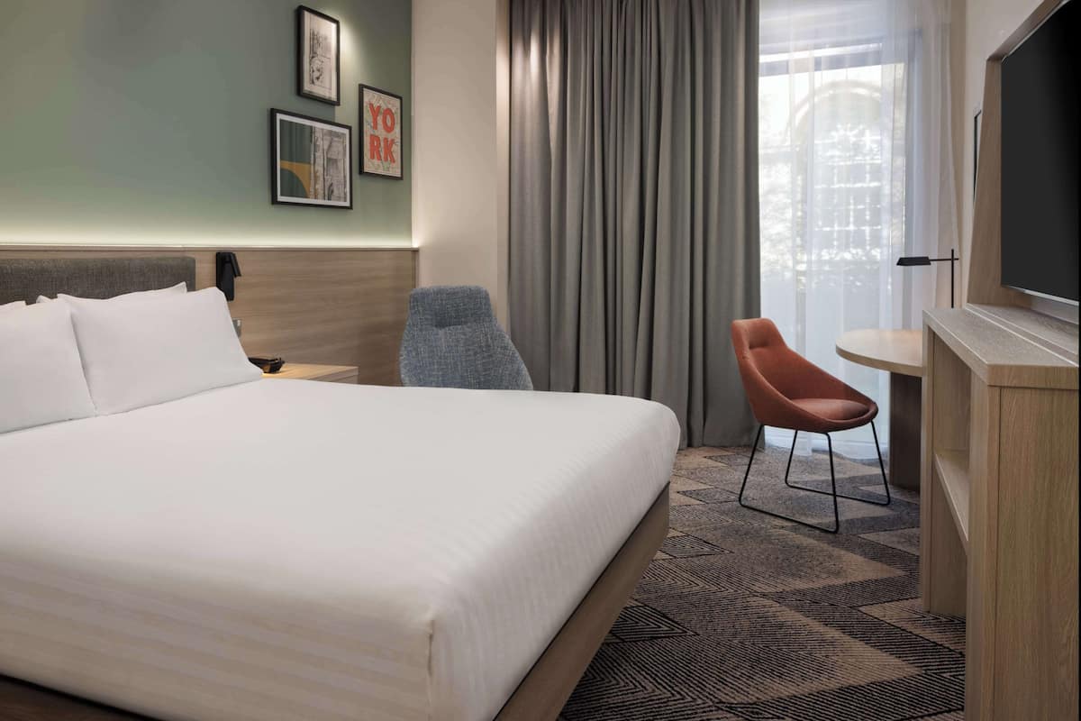 A hotel room with a large bed, a desk with a chair, a television, and a window with curtains.