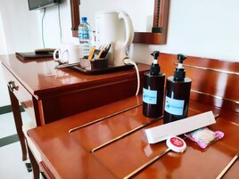 A hotel room with a wooden desk, a coffee maker, a water bottle, a cup, a tray with toiletries, and a mirror.