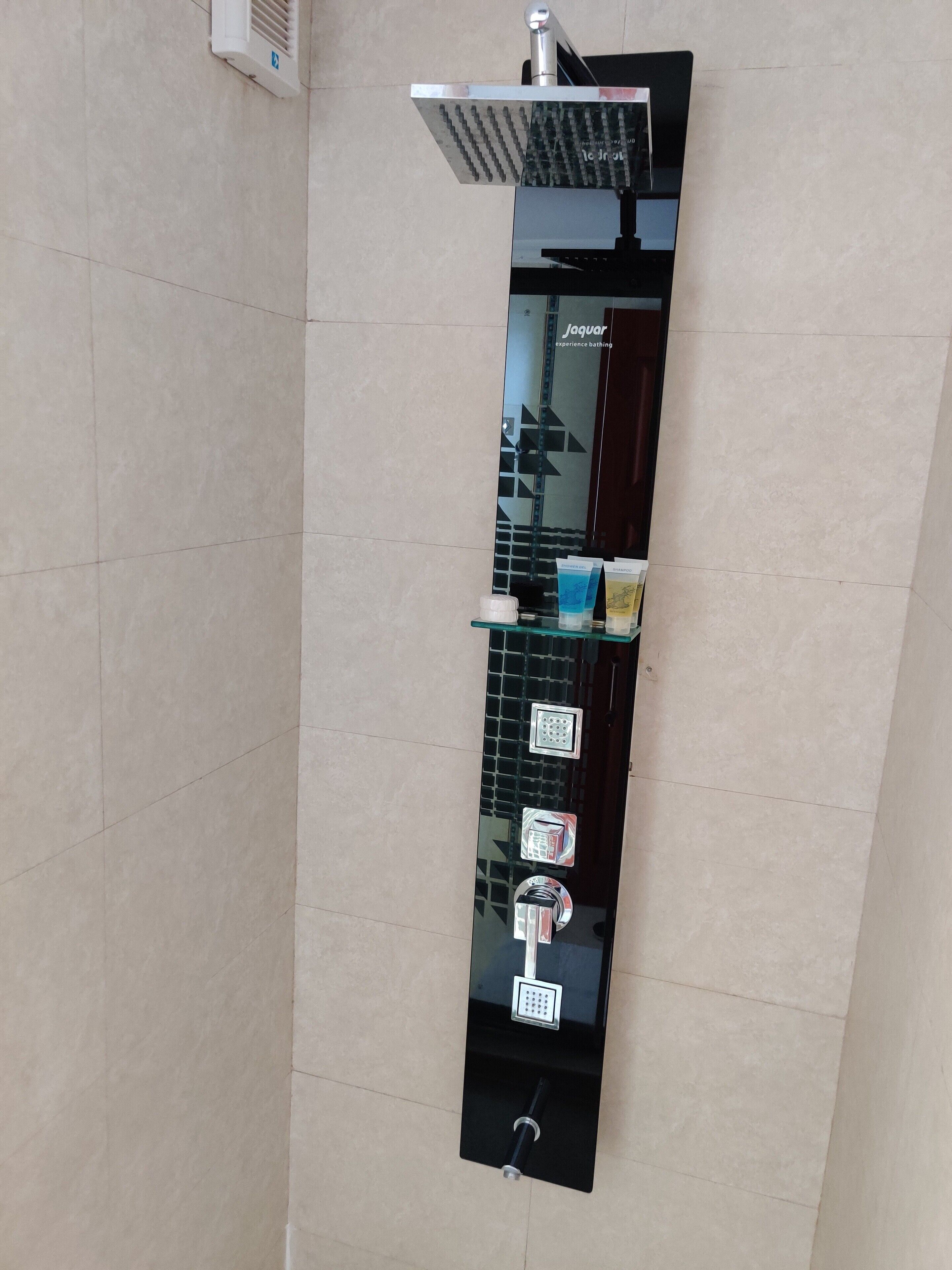 A modern bathroom with a vertical glass panel, a showerhead, and a control panel with buttons.