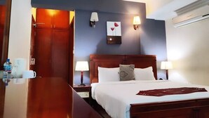 Habitación de hotel con cama de madera, dos lámparas de noche, una mesita de noche, una obra de arte colgada en la pared y una puerta que da a otra habitación.