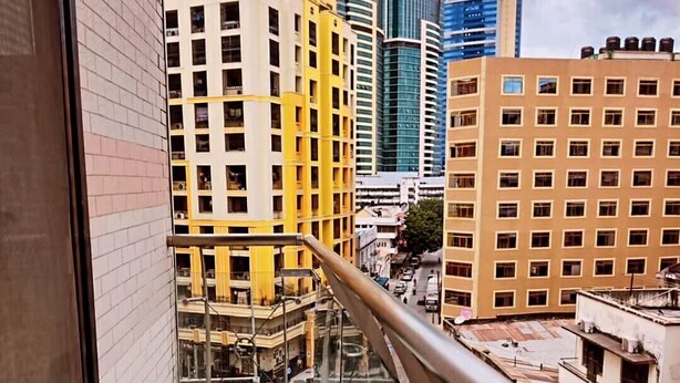 Vista desde un balcón con barandilla de vidrio que domina un paisaje urbano con edificios modernos.