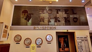 Un área de recepción con una araña, un cartel que dice "HOTEL NIKKO RECEPTION" y un panel con el tipo de cambio de divisas.