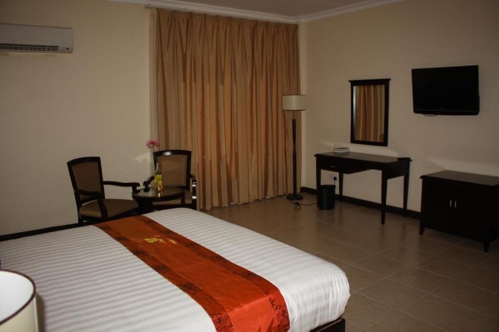 Una habitación de hotel con cama, escritorio, silla, televisor y cortinas.