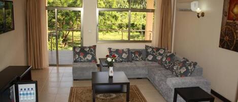 A living room with a sofa, a coffee table, and a TV stand with a mini-fridge.