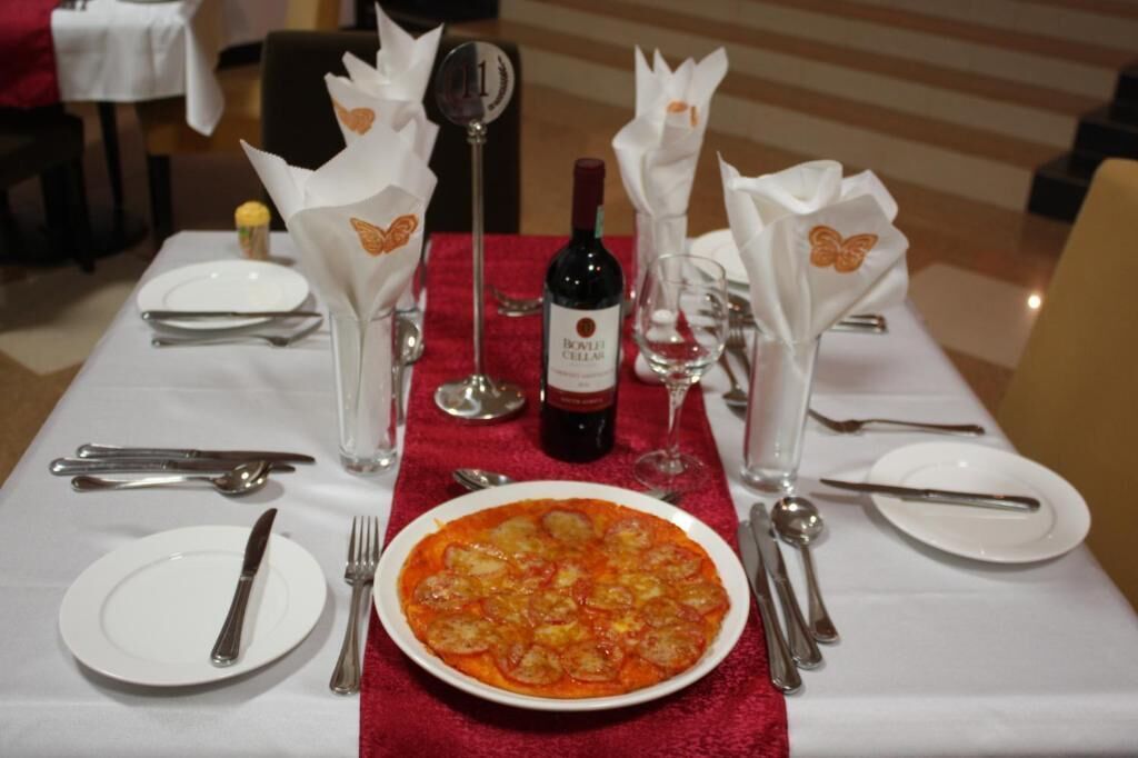 A dining table set with a red tablecloth, white plates, silverware, and a bottle of wine.