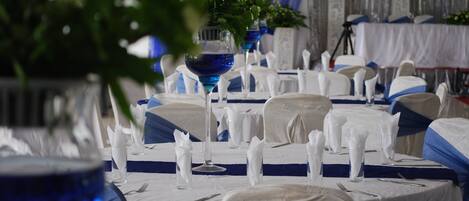 Un salón de banquetes con mesas redondas cubiertas con manteles blancos, listones azules y servilletas blancas.