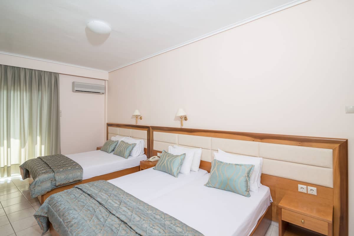 Habitación de hotel con dos camas, una mesita de noche, un equipo de aire acondicionado y una ventana con cortinas.