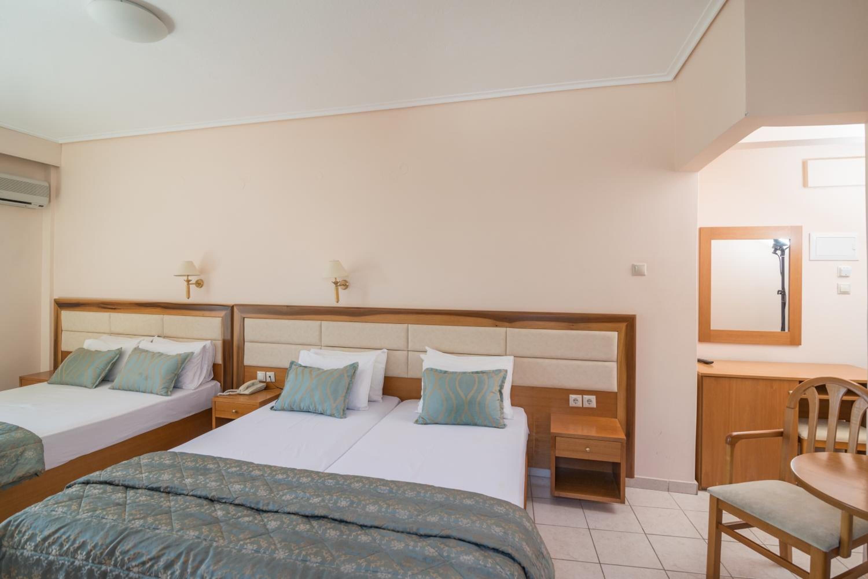 A hotel room with three beds, a desk, a chair, and a mirror.