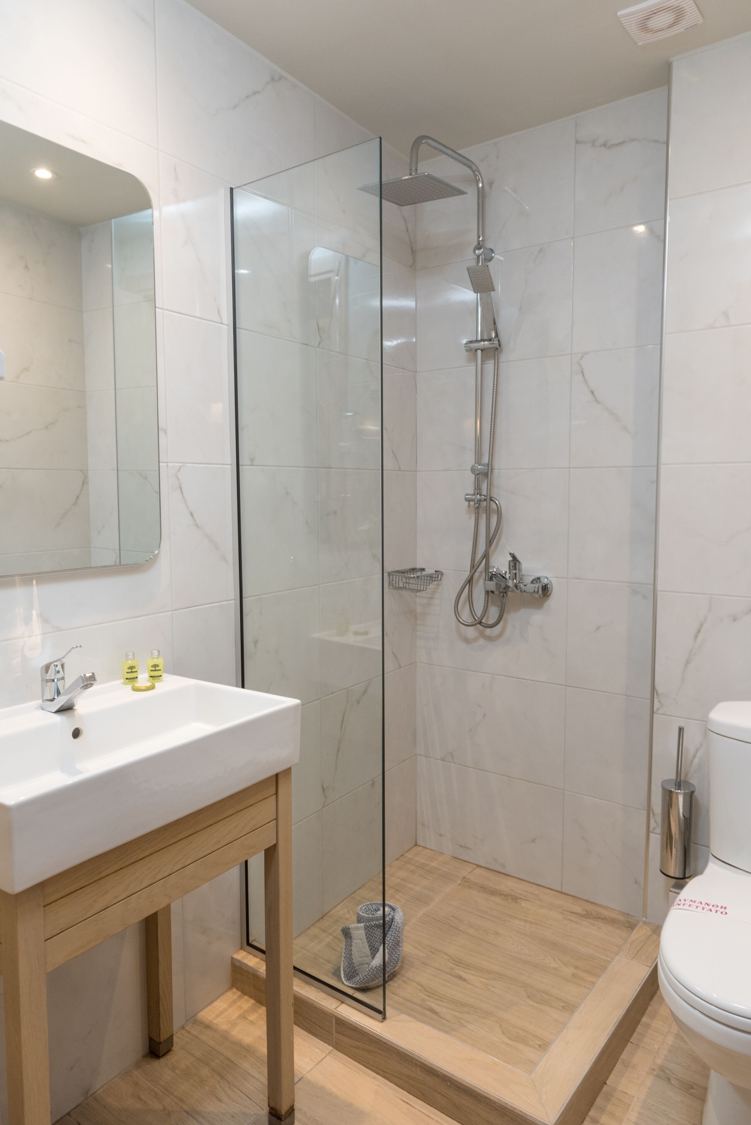 Une salle de bain moderne avec une douche à parois de verre, un lavabo blanc avec un meuble en bois et des toilettes.