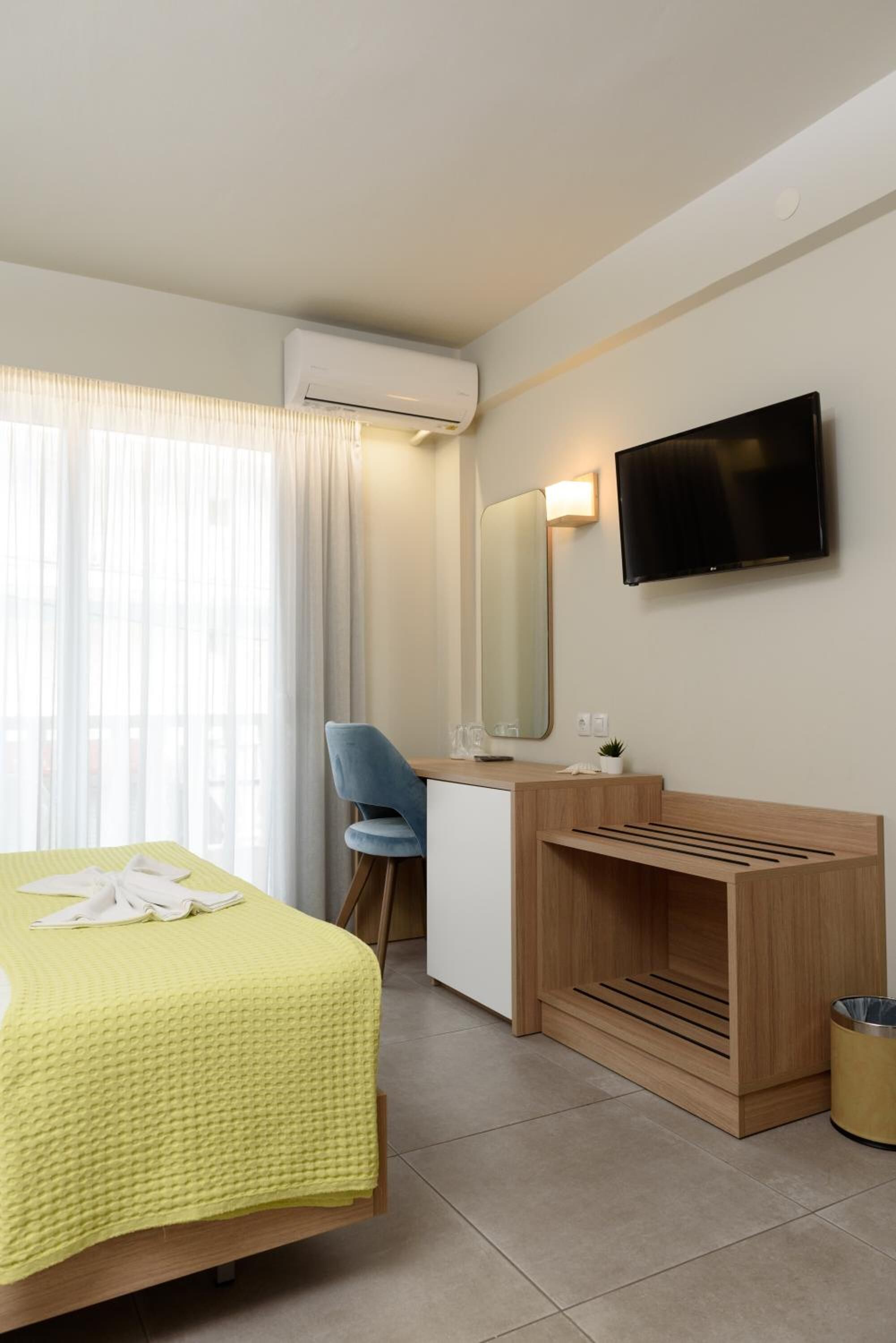 Una habitación de hotel con cama, escritorio, silla, televisor y aire acondicionado.