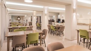 Un comedor amplio con varias mesas y sillas, una zona de cocina al fondo, y un diseño de interiores moderno.