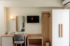 Una habitación de hotel moderna con escritorio, silla, televisión, espejo y armario.