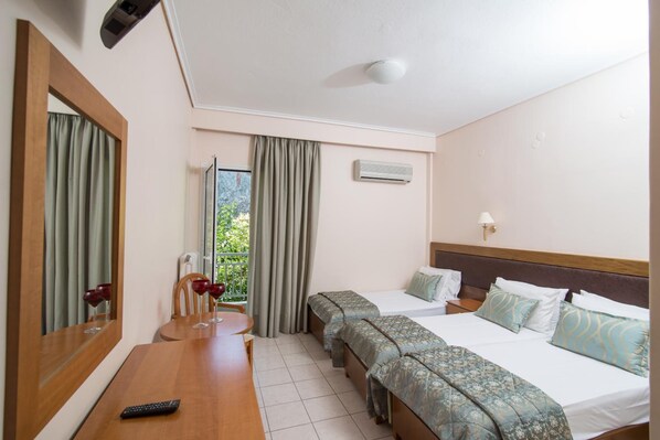 Habitación de hotel con cama, mesitas de noche, un espejo, ventana con cortinas, equipo de aire acondicionado y un control remoto sobre la mesa.
