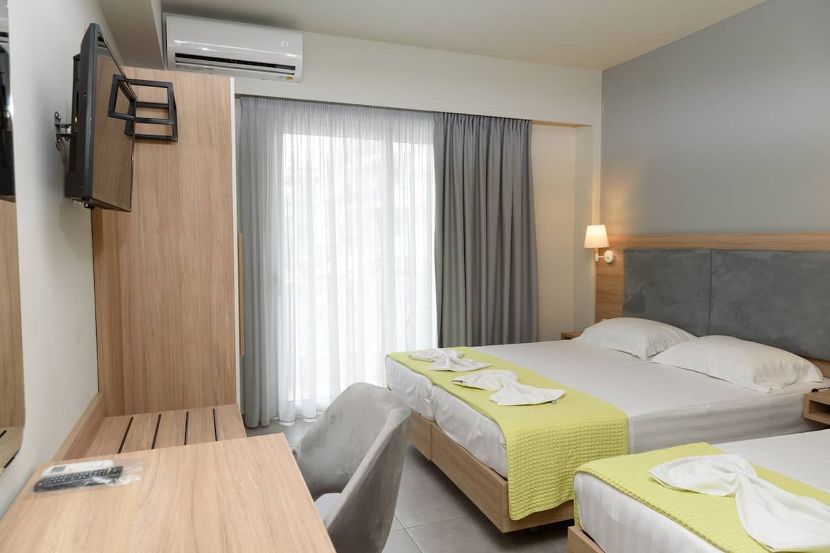 Habitación de hotel con dos camas, un escritorio, una silla, televisor montado en la pared y un equipo de aire acondicionado.