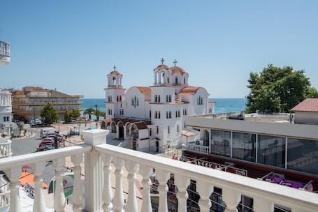 A white building with multiple domes and a balcony overlooking a coastal area.