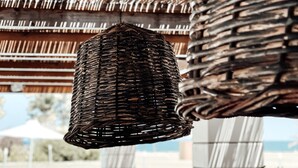 A wicker hanging light fixture and a woven basket in an outdoor setting with a pool and lounge chairs. - Dion Palace Resort & Spa by Anayia All Inclusive Resorts (Dio-Olympos)