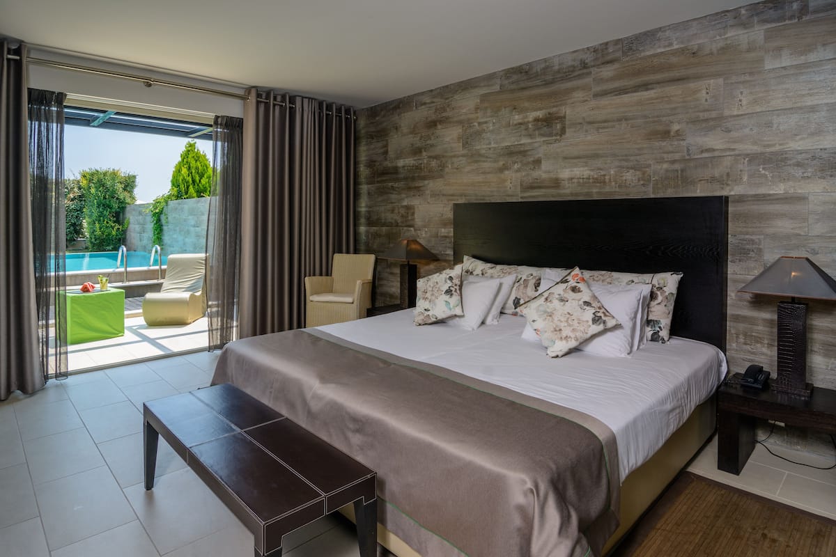 A modern bedroom with a large bed, a bedside table, a lamp, and a view of an outdoor pool area.