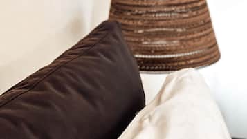 A room with a hanging woven lamp and two pillows, one dark and one light, on a white wall.
