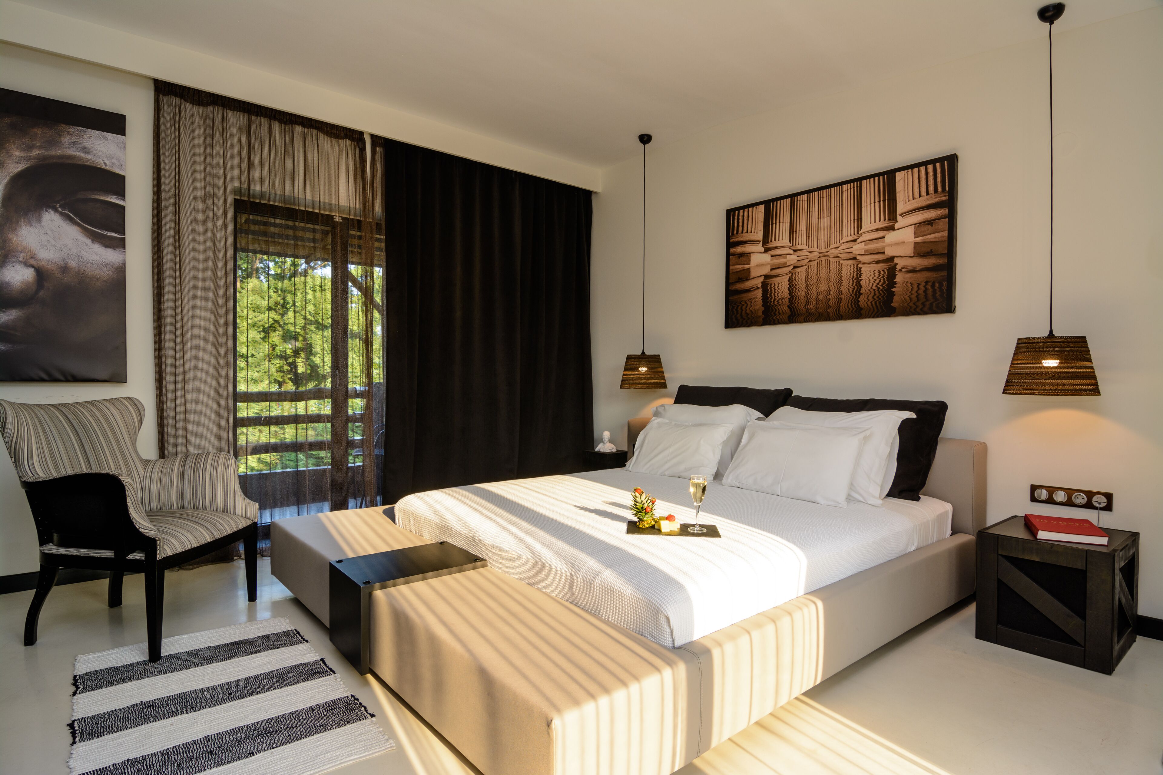 Een moderne slaapkamer met een groot bed, een stoel, een nachtkastje en uitzicht op groen.