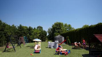 Children can play on the swing set, slide, and castle-like playhouse in this outdoor play area surrounded by trees.