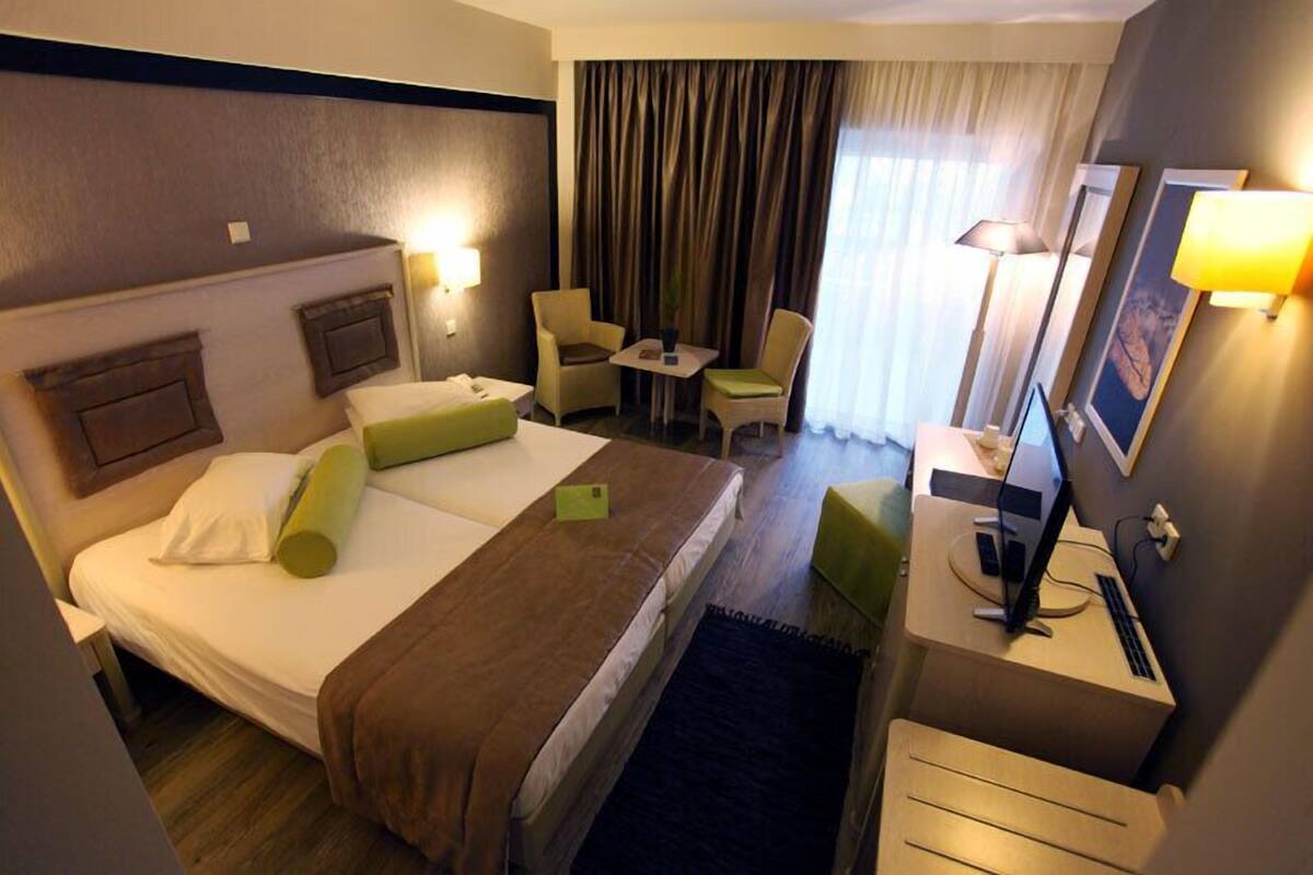 A hotel room with a large bed, a desk with a computer, a chair, a small table, and a TV.