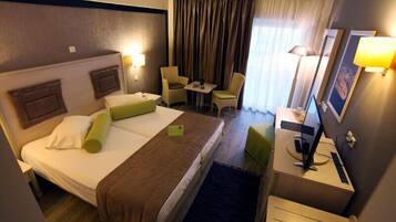 A hotel room with a large bed, a desk with a computer, a chair, a small table, and a TV.