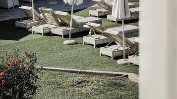 A rooftop lounge area with sun loungers and umbrellas, surrounded by a building with a tiled roof and a covered patio.
