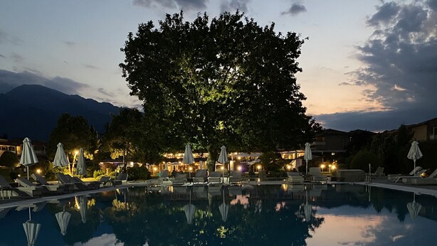 A pool area with lounge chairs and umbrellas, surrounded by trees and buildings. - Dion Palace Resort & Spa by Anayia All Inclusive Resorts (Dio-Olympos)