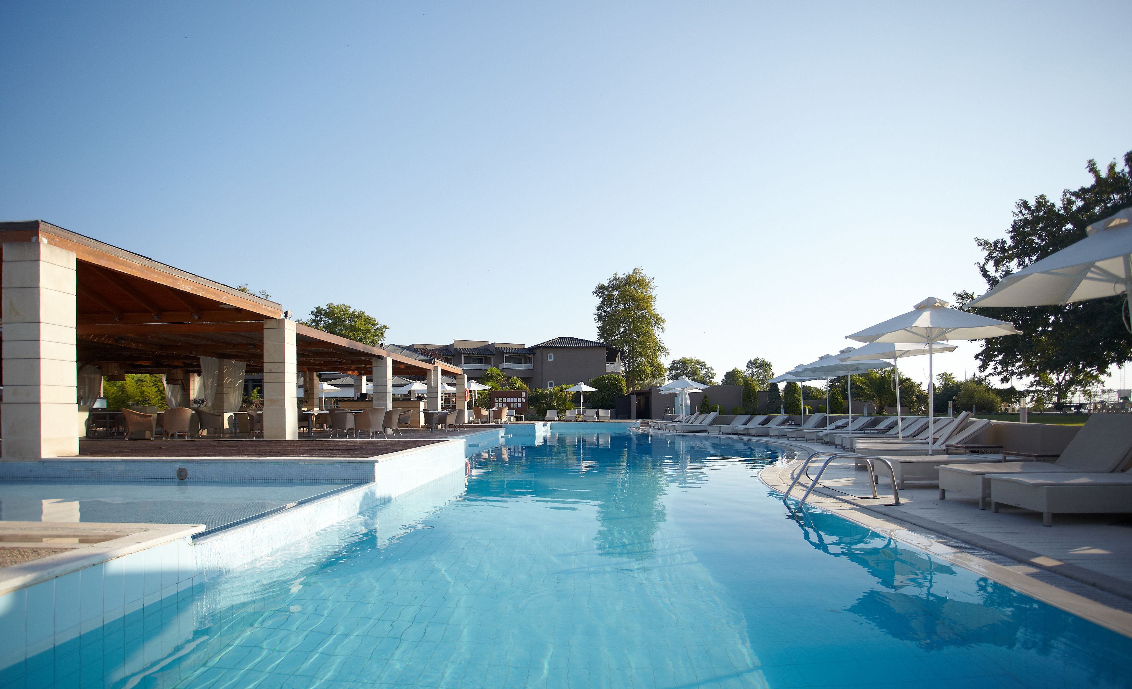 Une piscine entourée de bâtiments et d’arbres, avec des chaises longues et des parasols.