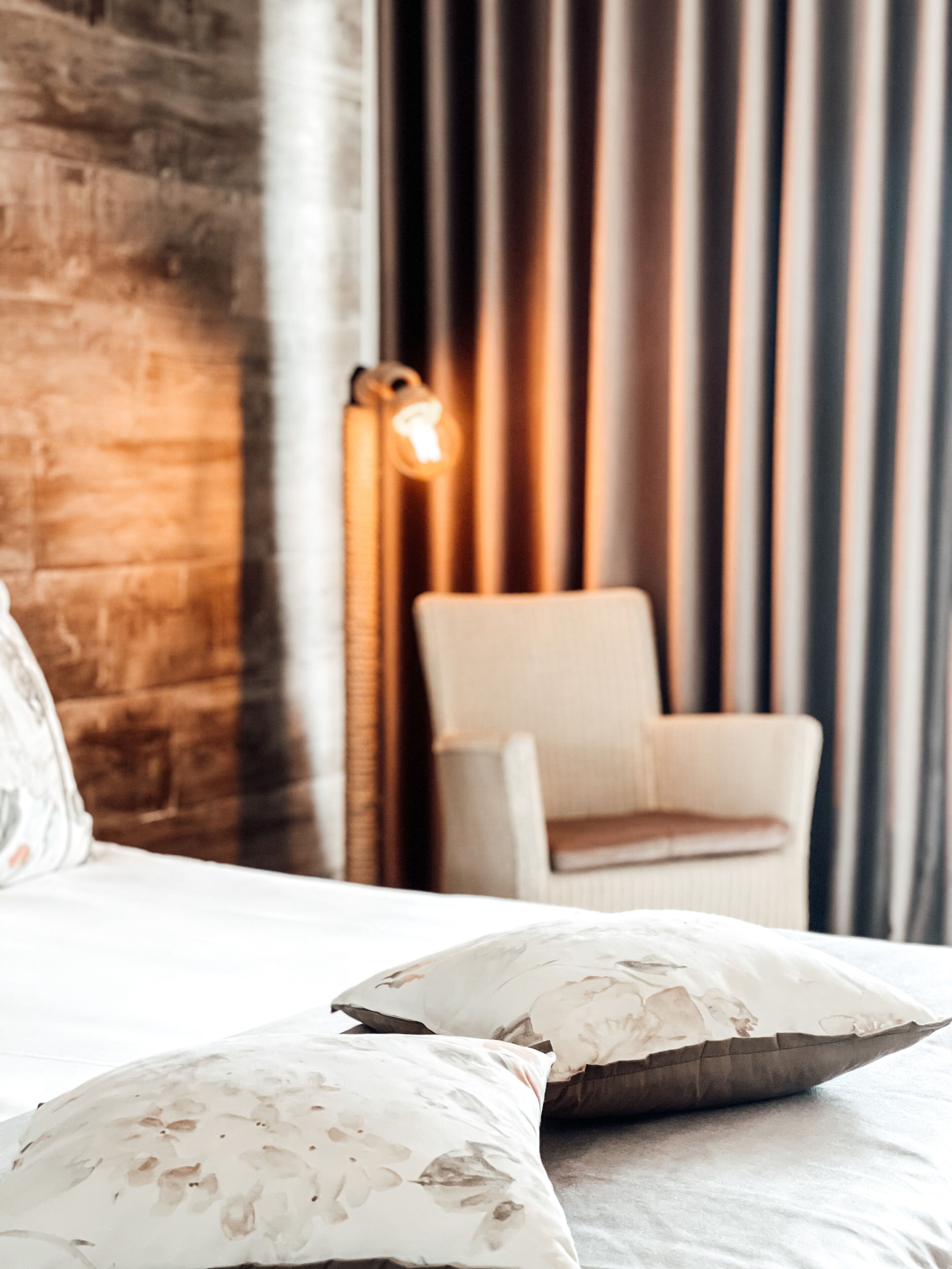 A hotel room with a wooden accent wall, a white armchair, and a bedside lamp.