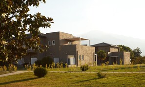 A modern two-story building with a flat roof, a covered outdoor area, and a well-maintained lawn with young trees.