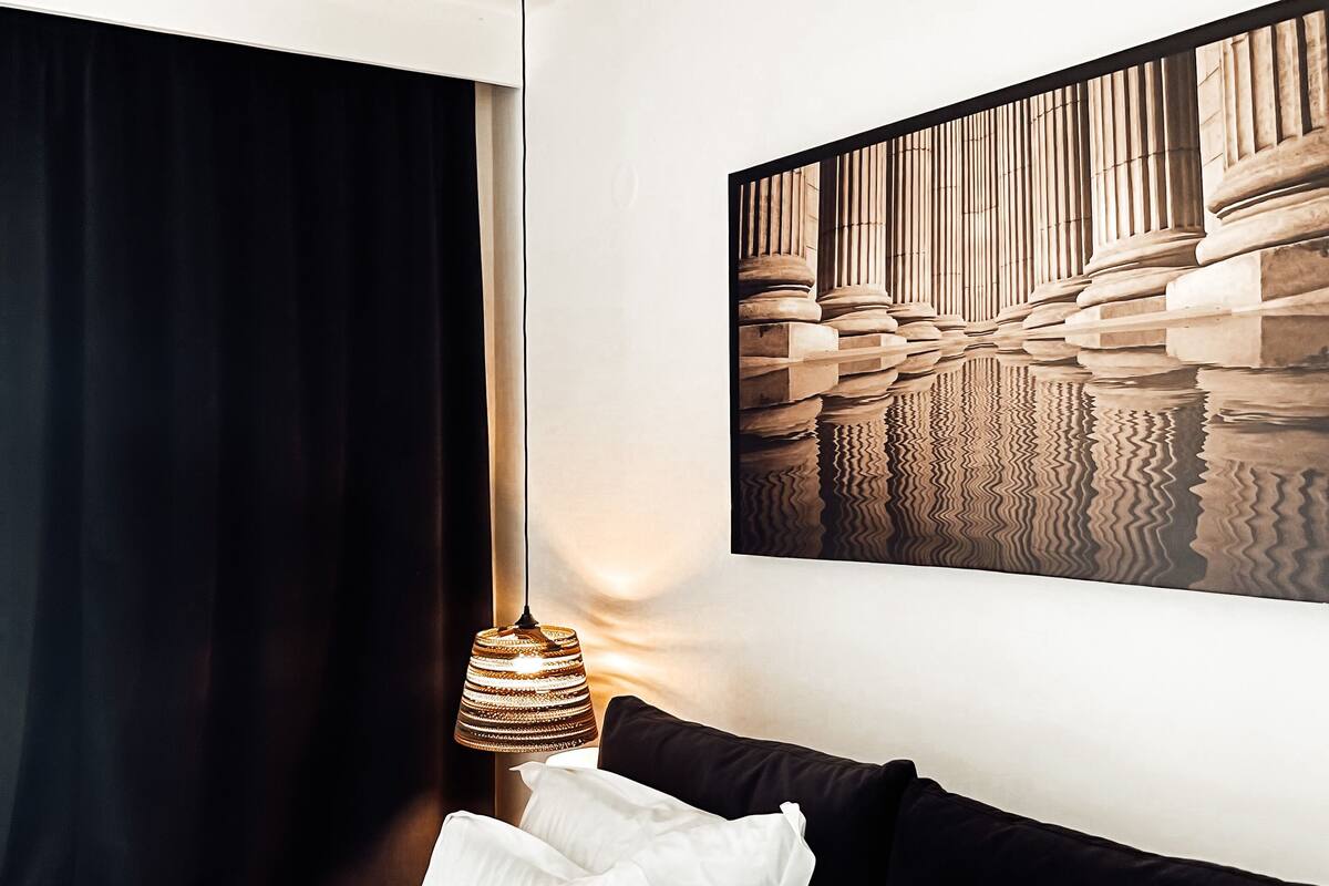 A modern hotel room with a large bed, black and white bedding, a hanging lamp, and a wall-mounted artwork.