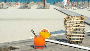 A beach scene with a drink and a woven basket on a wooden deck. - Dion Palace Resort & Spa by Anayia All Inclusive Resorts (Dio-Olympos)