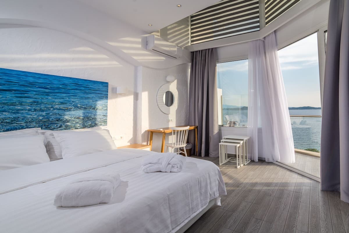 A modern hotel room with a large bed, a desk, and a view of the sea.